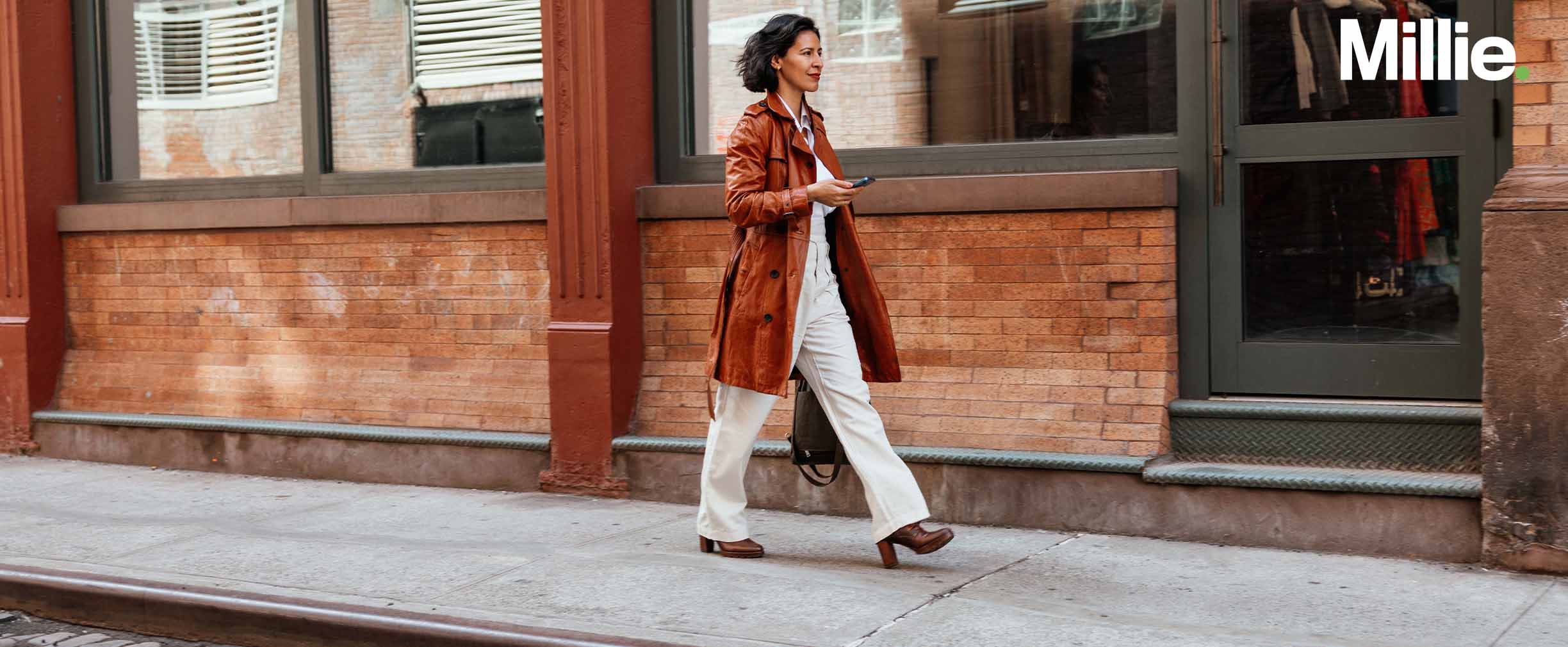 A smiling woman walking down the street and holding her phone.