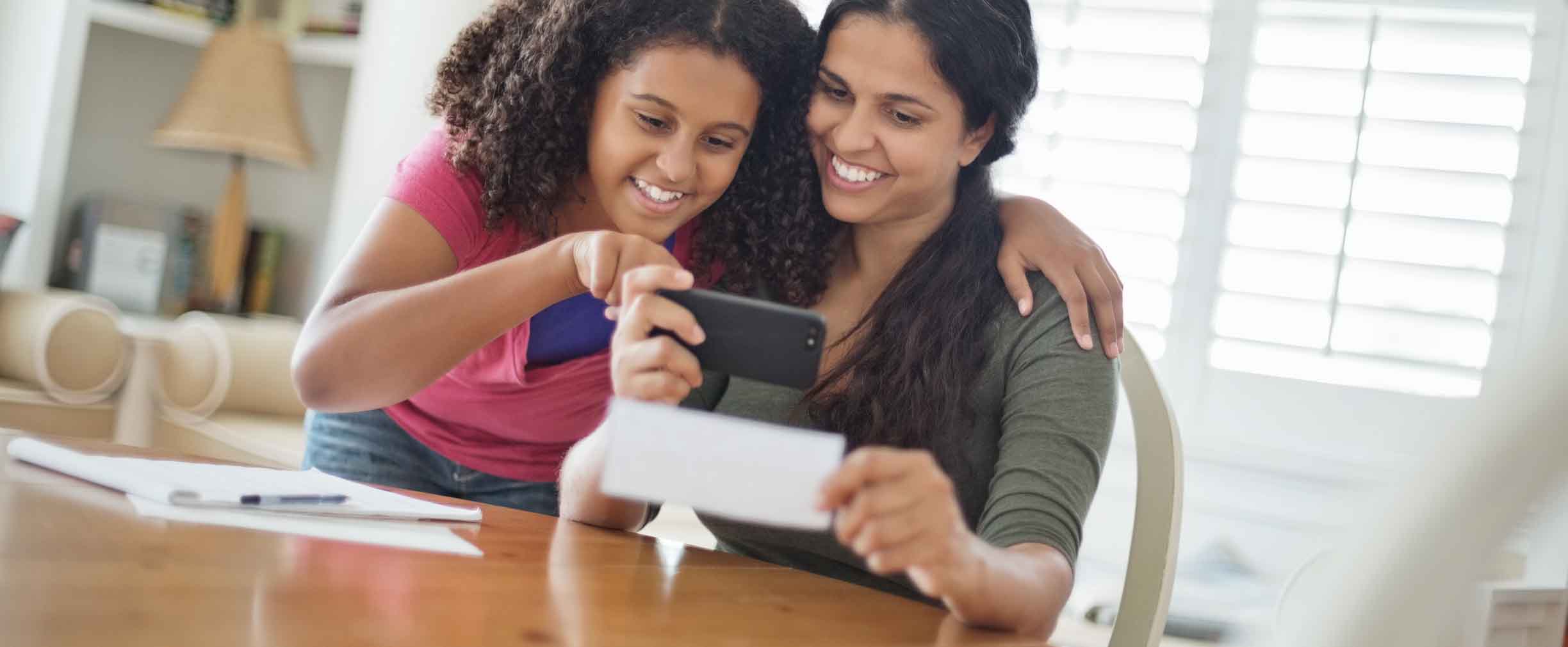 daughter assisting mother to deposit check through smart phone