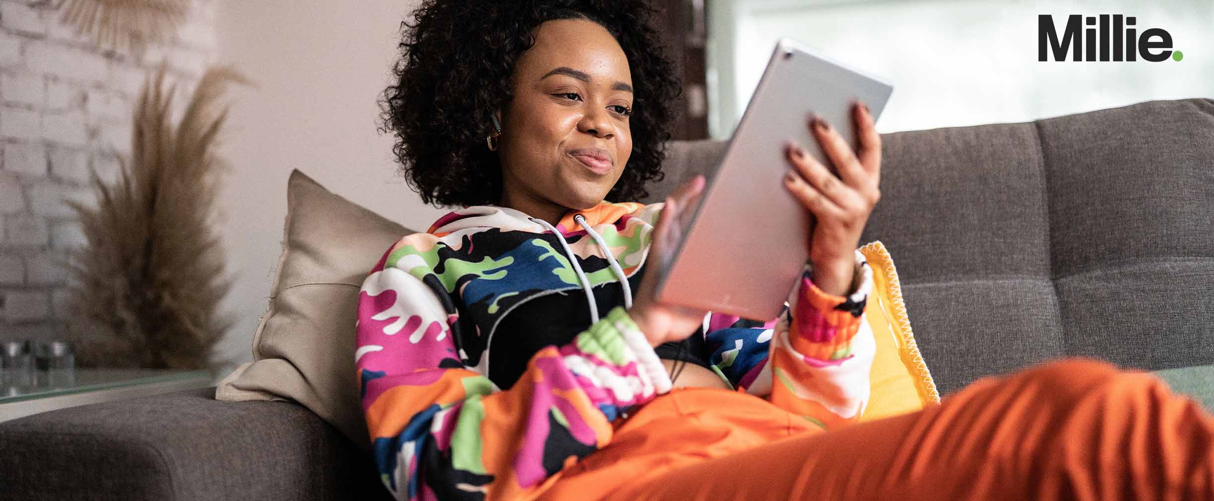 A young woman sitting on a couch looking at her tablet. 