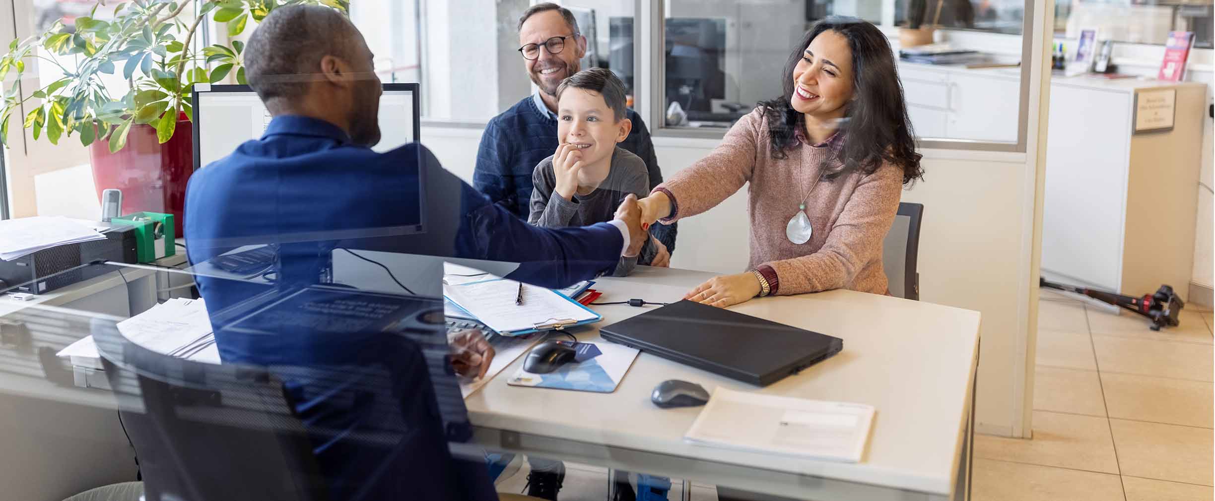 A husband and wife and their grade-schooler shake hands with a banker in a plant-filled sunlit office