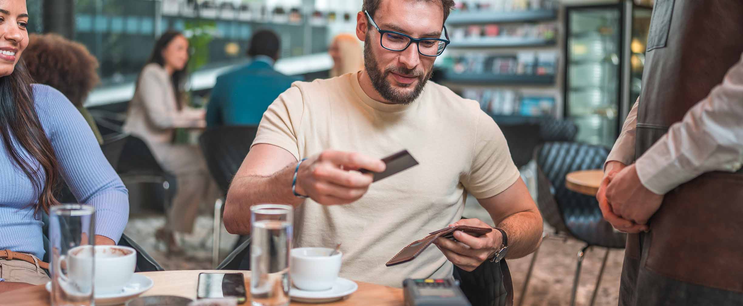 A man in glasses takes his credit card out of his wallet to pay for a meal at a modern restaurant