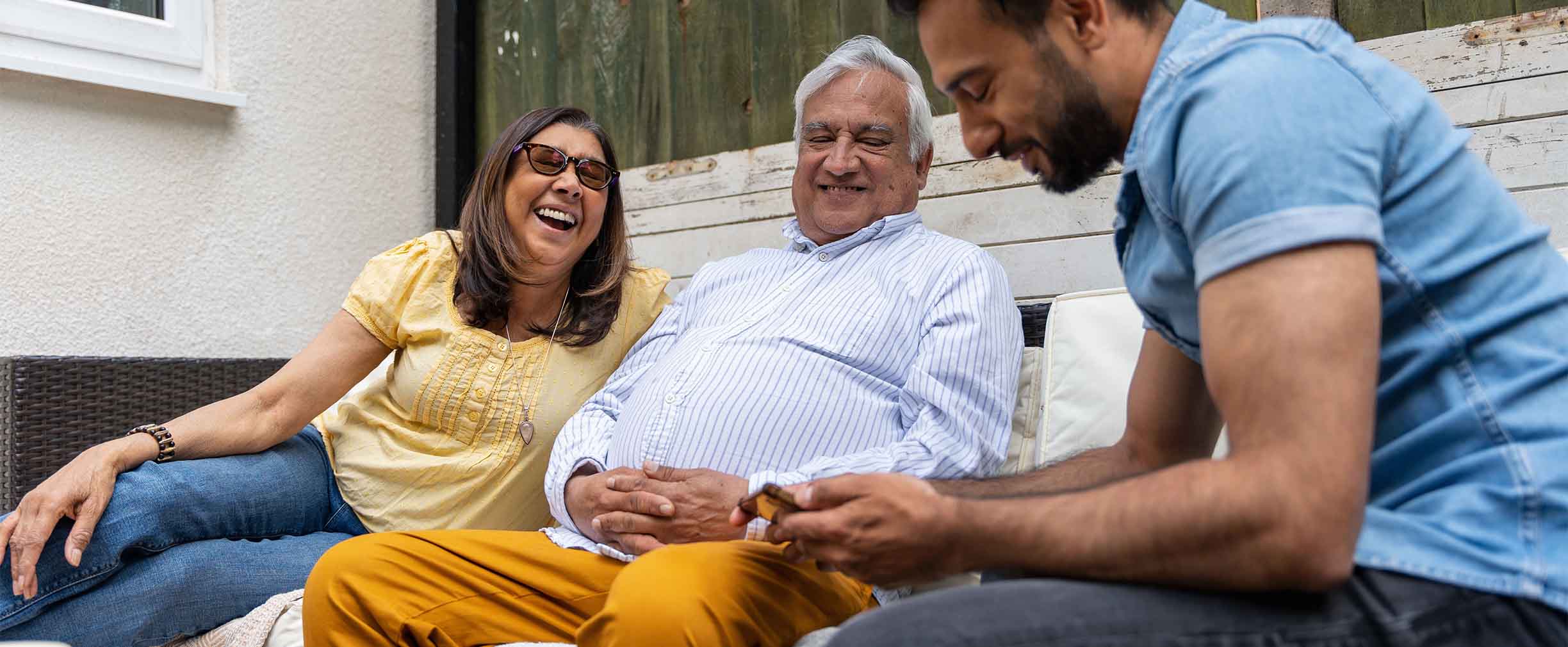 A young adult laughing and smiling with two older family members on a rustic patio