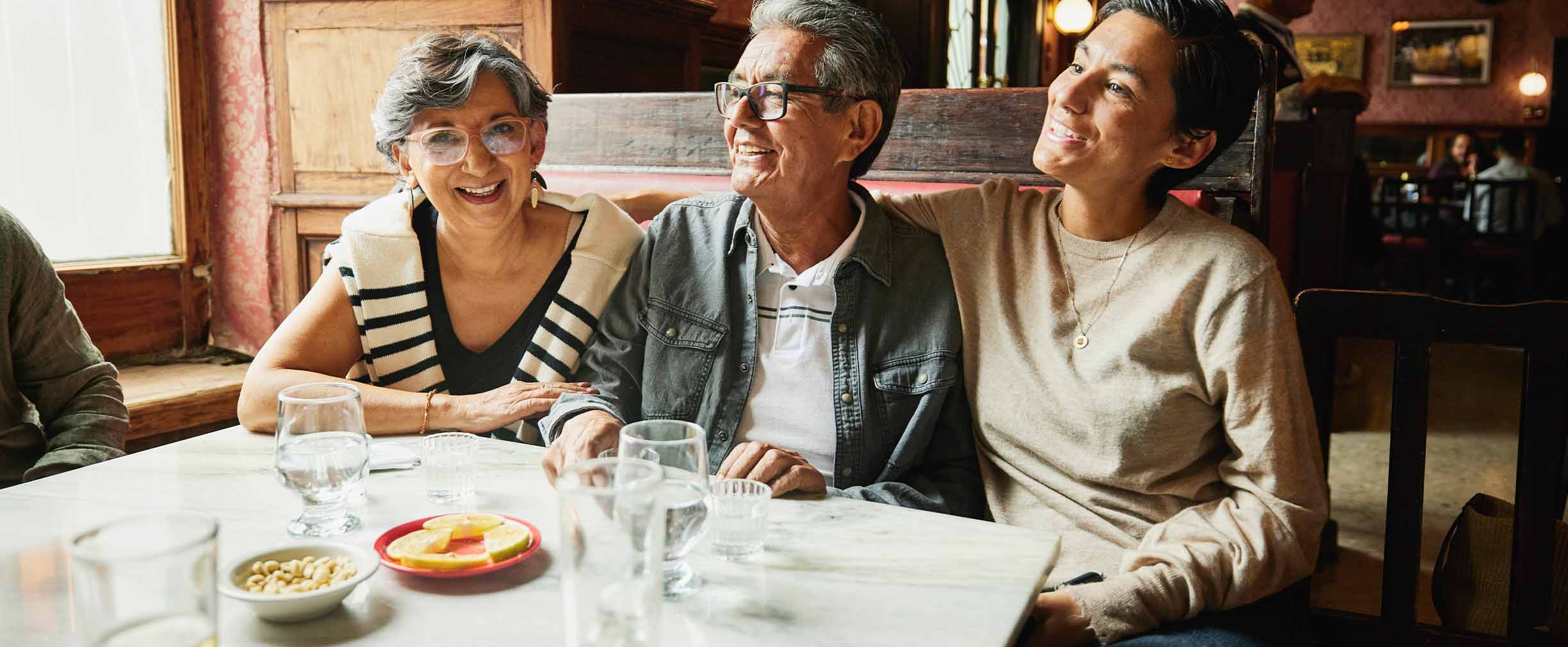 A woman sits in a sunny restaurant booth with her smiling parents