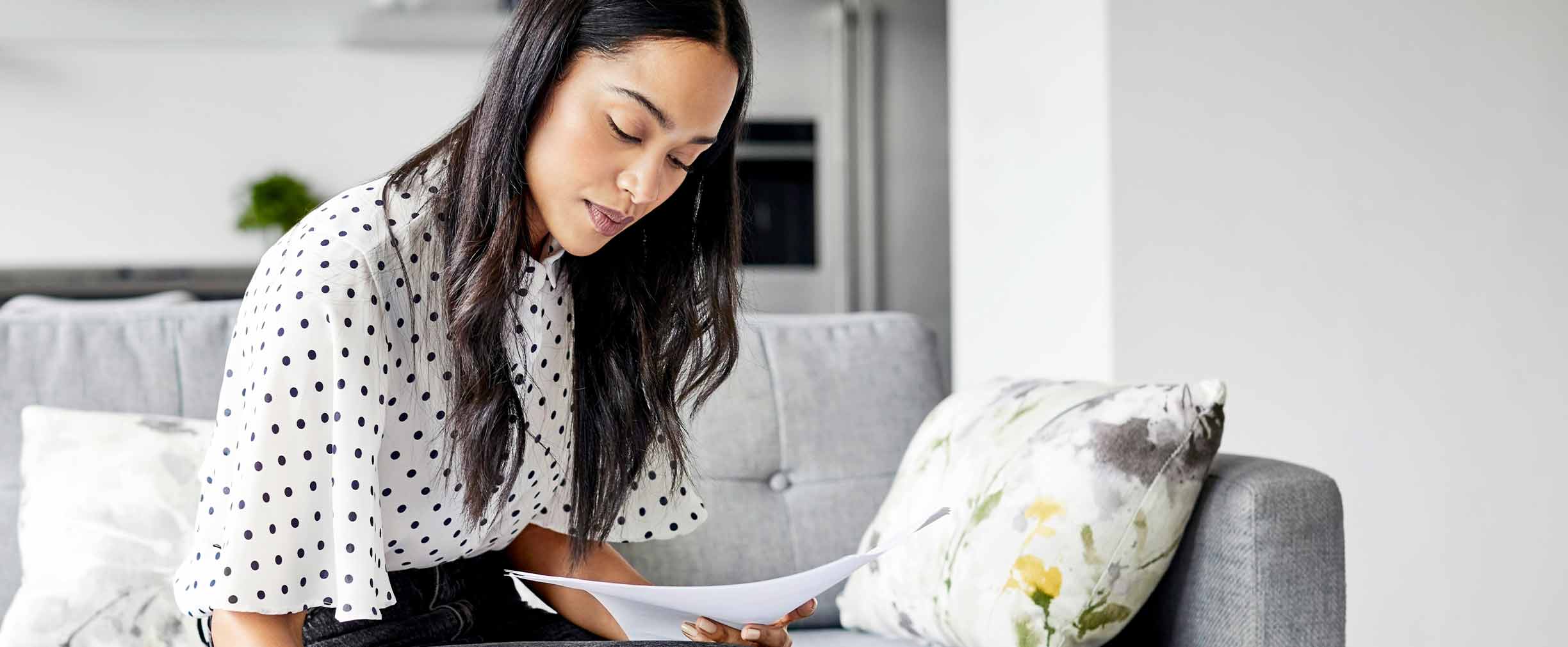 Young woman analyzing bills while writing in diary.Female is using digital tablet at table. She is sitting on sofa at home.