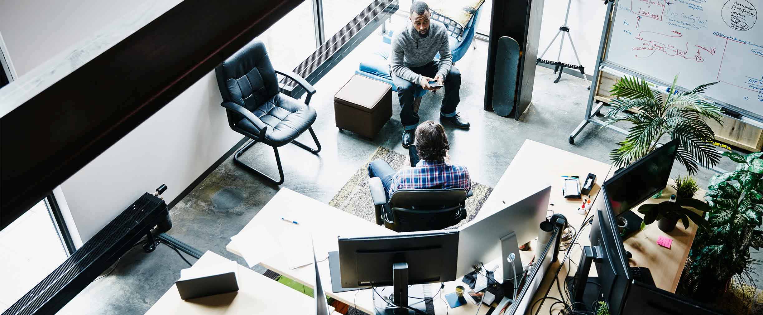 A bird’s-eye view of two people having a serious discussion in a bright, plant-filled office