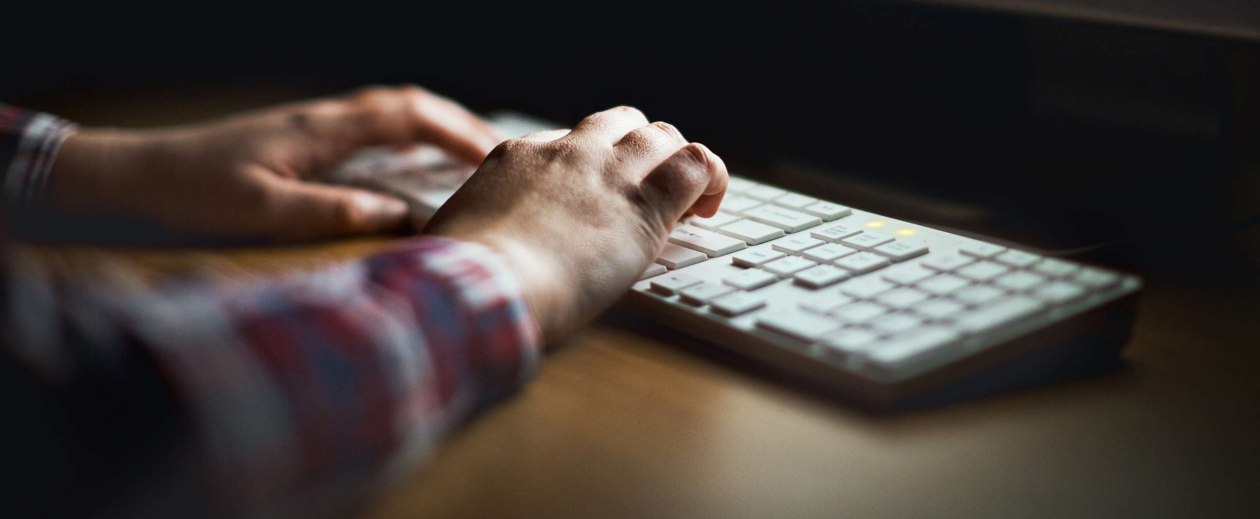 Hands type on computer keyboard lit by monitor